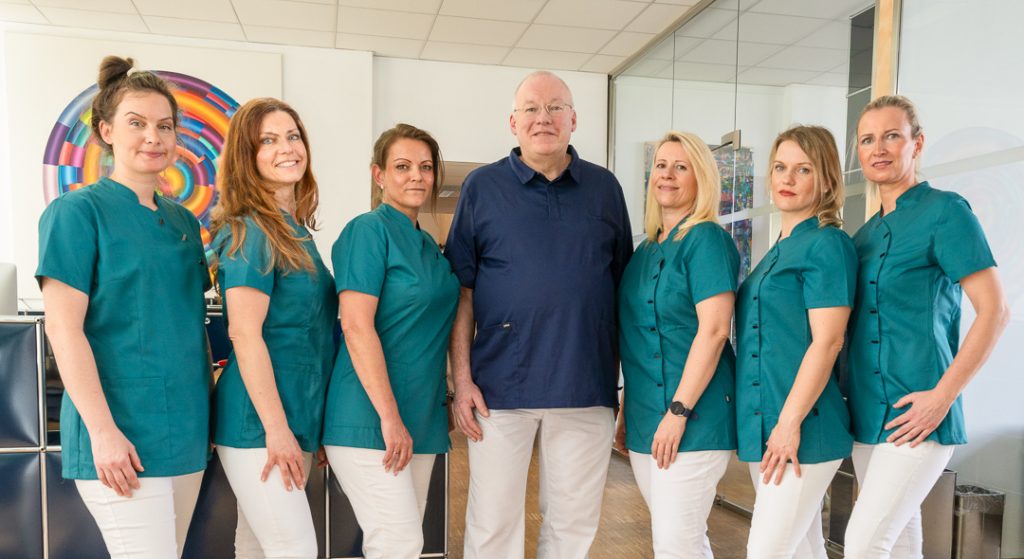 Foto einiger Praxismitarbeiterinnen mit Hartmut Benthin an der Rezeption.